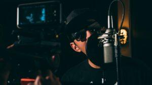 man in black cap and black framed sunglasses in front recording microphone