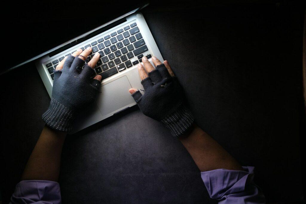 A person wearing fingerless gloves typing on a laptop on a dark surface